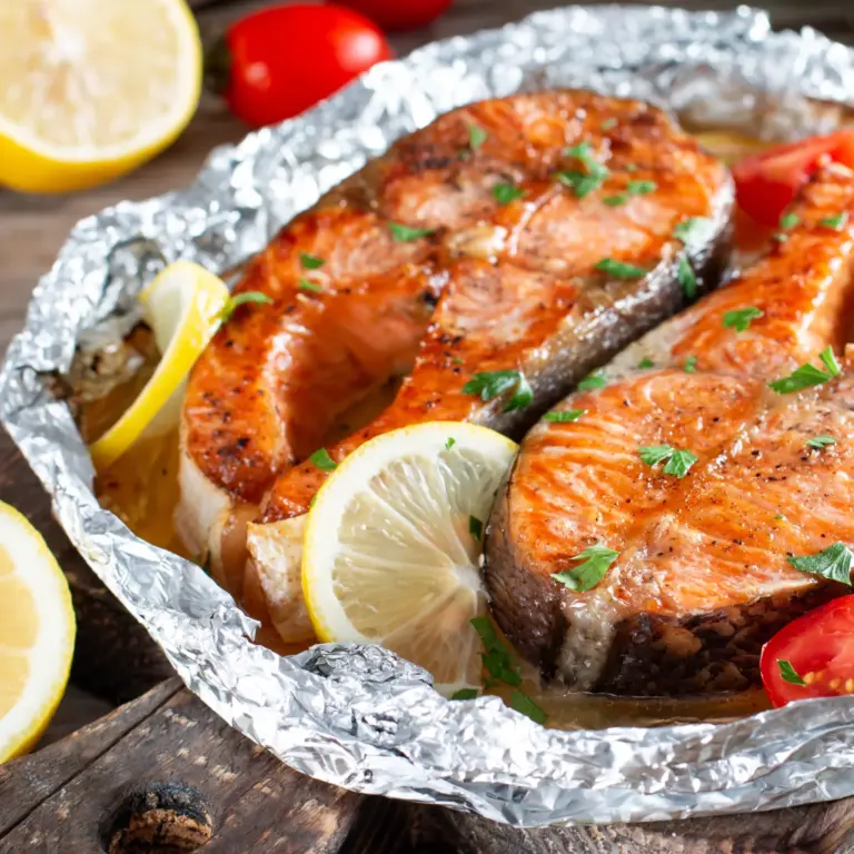 Gebackener Lachs - Two grilled salmon steaks with salt, pepper, lemon, tomato and parsley on a rustic wooden table